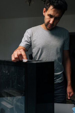 Vertical portrait of technician male wiping computer case, removing dust and grime for maintaining...