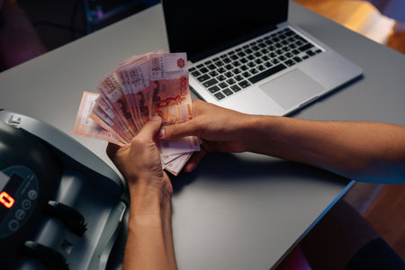 Close-up top view of cashier counting Russian rubles banknotes while working sitting at desk with...