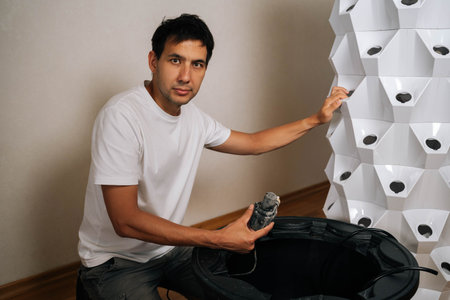 Home gardener assembling hydroponic tower garden, placing water pump inside water tank, creating...