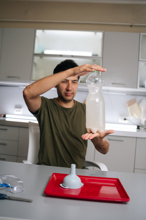 Home gardening enthusiast male mixing homemade liquid fertilizer in kitchen, combining bottles,...