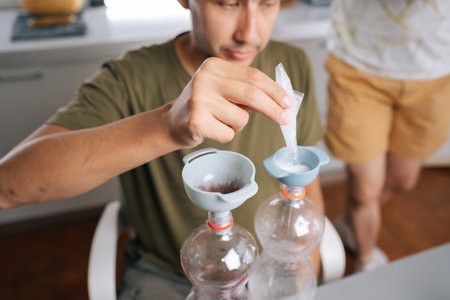 Cropped shot of urban farmer pouring fertilizer components into plastic bottles through funnels,...