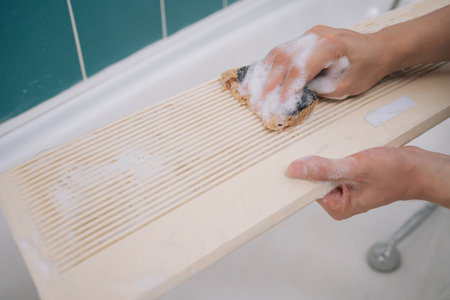 Cleaning detachable air conditioner filter with sponge, housekeeper maintaining hygienic bathroom...