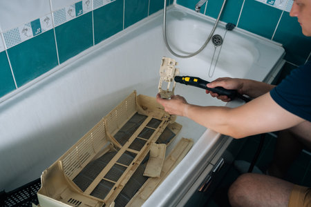 Top view of technician cleaning filter of air conditioner unit inside bathtub, utilizing steam cleaner to remove dirt and grime, ensuring optimal performance and hygiene.の写真素材