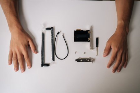 Close-up high-angle view of male hands carefully unpacking new wi-fi module from packaging on white desk, preparing for upcoming computer upgrade or installation process.の写真素材