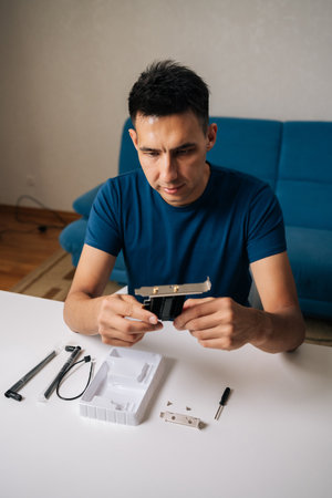Vertical portrait of skilled technician male assembling wi-fi module using tools at home office desk, focusing on intricate components and ensuring proper connection. Concept of desktop PC maintenanceの写真素材
