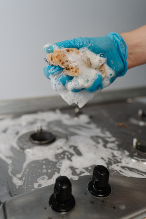 Vertical cropped shot of man wearing protective gloves squeezing soapy water from sponge during...