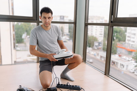 Professional window cleaner kneeling, holding robotic cleaning device, looking at camera by...