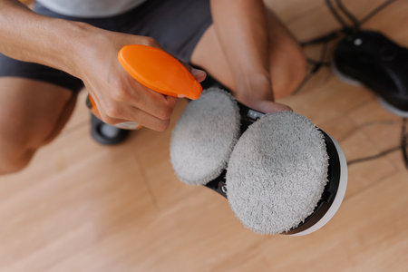 Close-up cropped shot of unrecognizable worker preparing automatic cleaning robot by spraying detergent on cleaning pads, ensuring streak-free and efficient window cleaning.の写真素材