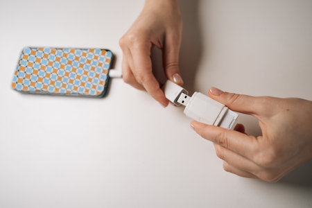 Woman hands connecting USB flash drive to smartphone using adapter cable sitting at white table, transferring data or charging device, close-up. Concept of modern technology.の写真素材