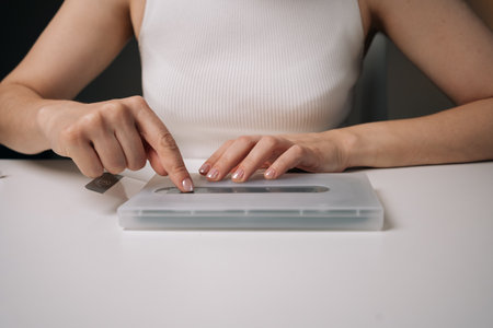 Close-up of technician female using specialized machine to precisely apply protective glass film onto smartphone screen, ensuring maximum coverage and protection against scratches and damage.の写真素材