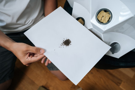 Agricultural technician holding paper with seeds, preparing for planting in modern hydroponic system with rockwool and hydroponic tower in background. Concept of healthy and sustainable cultivation.の写真素材