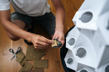 Top view of gardener placing piece of rockwool into net pot, preparing for planting in modern hydroponic tower garden system, promoting sustainable and efficient urban farming practices.の写真素材