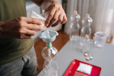 Close-up hands of unrecognizable gardener pouring organic fertilizer into plastic bottle using...