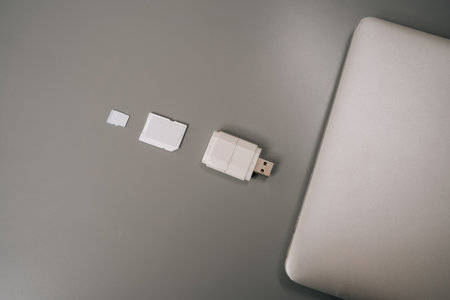 Card reader with micro sd card lying on gray table next to white laptop, composing flat lay still life representing storing, transferring and managing digital data. Concept of computer hardwareの写真素材