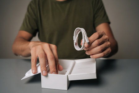 Detail cropped shot of unrecognizable man sitting at table unboxing new electronic device, holding...