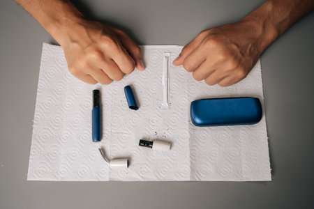 Close-up top view of unrecognizable man cleaning electronic cigarette with cleaning stick and paper on table, performing maintenance, ensuring proper hygiene, sanitizing personal vaping equipment.の写真素材