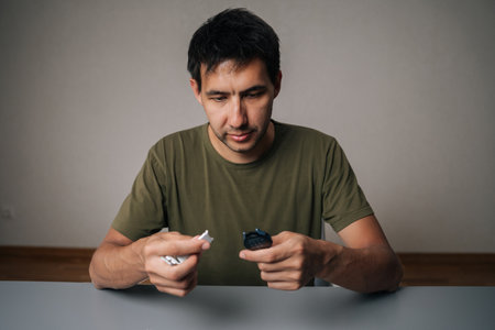 Focused male maintaining personal device hygiene, disinfecting modern smartwatch with antibacterial spray, sitting at table on gray isolated background. Concept of healthy lifestyle.の写真素材