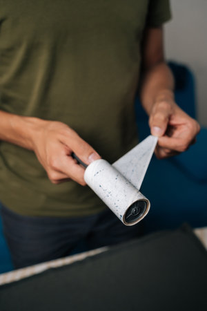 Vertical cropped shot of man peeling off used layer of sticky lint roller, preparing to clean clothes from dust, hair and fibers, ensuring garments remain tidy and fresh. Concept of household chores.の写真素材
