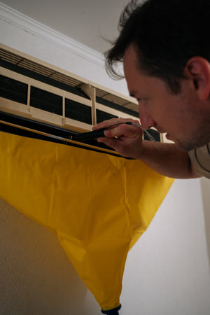 Close-up vertical shot of HVAC technician using flashlight, inspecting air conditioning unit covered with yellow drop cloth during maintenance or repair service. Concept of air condition maintenanceの写真素材