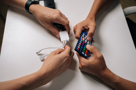 Close-up top view of two technicians connecting RGB led strip lights using remote control and controller, adjusting backlight settings for customized illumination. Concept of modern technology.の写真素材