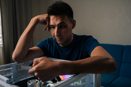 Pensive technician male upgrading desktop computer by installing wi-fi module, focusing intently on task with thoughtful expression, showcasing expertise and attention to detail at workshop.の写真素材
