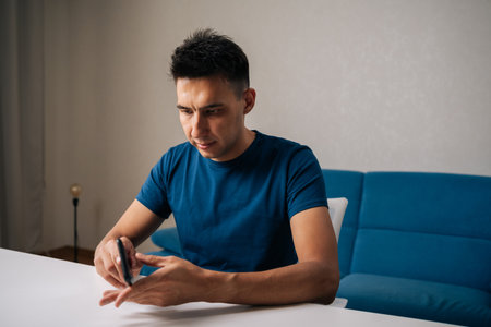 Portrait of focused young man inserting smartphone into protective case, ensuring secure fit sitting on white table at home. Concept of phone maintenance and serviceの写真素材