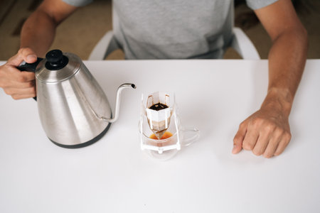 Cropped shot of person brewing drip coffee with kettle, carefully pouring hot water over paper...