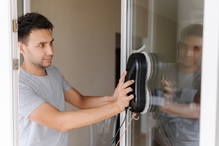 Young man installing robotic vacuum cleaner on window, preparing to activate device for efficient...