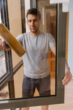 Vertical portrait of focused window cleaner male wiping glass surface with squeegee, removing dirt...