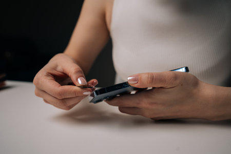 Close-up view of woman removing damaged tempered glass screen protector from smartphone with...