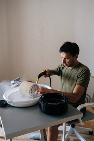 Vertical portrait of man cleaning humidifier filter with steam cleaner, ensuring clean and healthy air in home, demonstrating importance of regular maintenance for optimal performance and hygiene.の写真素材