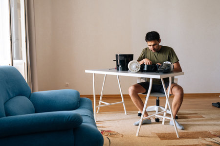 Remote wide shot of young man disassembling and cleaning air humidifier filter sitting at table in...