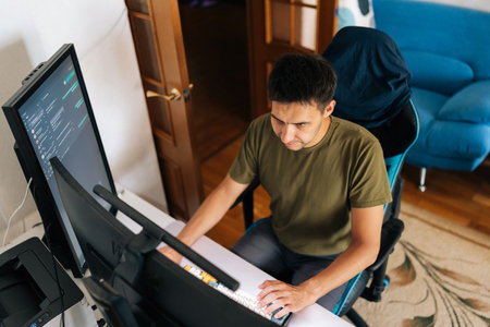 Top view of programmer male working from home office using multiple monitors setup and typing on mechanical keyboard looking to screen while sitting on gaming chair. Concept of remote workplace.の写真素材