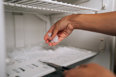 Cropped shot of man using knife to remove ice buildup from inside refrigerator, highlighting concept of defrosting and kitchen maintenance. Concept of domestic work, housekeeping and household.の写真素材