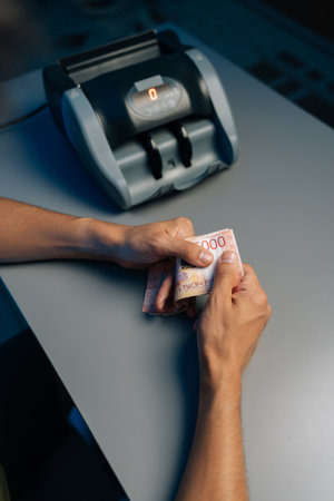 Close-up top view of cashier counting Russian rubles banknotes late at night after closing store using money counting machine in background. Concept of financial accounting in modern office.の写真素材