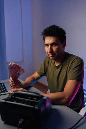 Vertical portrait of professional cashier male counting money, verifying banknotes using laptop and...