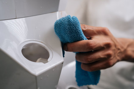 Close-up hands of unrecognizable person cleaning white system with rag, ensuring optimal conditions...