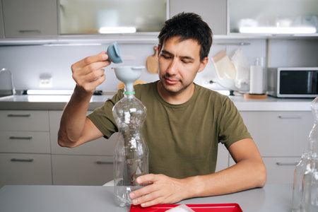 Plant researcher male pouring organic fertilizer through funnel into plastic bottle, preparing...
