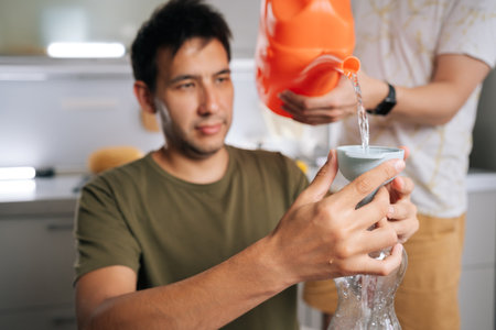 Two plant researcher enthusiast preparing fertilizer for plants in home kitchen, mixing water and nutrients in plastic bottle using funnel and watering can. Concept of healthy sustainable cultivation.の写真素材