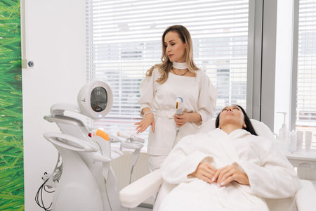 Female patient receiving professional facial treatment in beauty salon, undergoing hardware mesotherapy and microneedling to rejuvenate skin, achieve anti-aging effect in modern cosmetology clinic.の写真素材