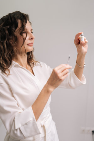 Vertical portrait of healthcare worker drawing medication from vial into syringe, getting ready for vaccination or cosmetic treatment in clinical environment. Concept of beauty, facial anti-aging.の写真素材