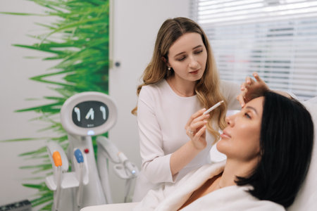 Side view of middle-aged woman receiving facial aesthetic procedure featuring cosmetologist marking...