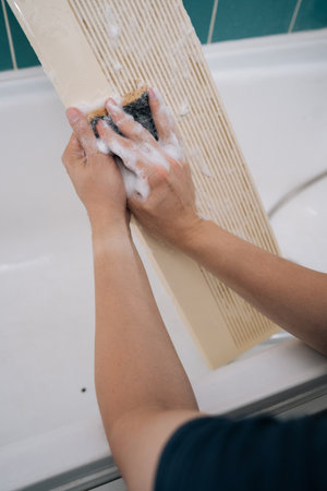 Close-up of housekeeper diligently cleaning detachable air conditioner filter using sponge and soap, ensuring dust-free and healthy environment within bathroom. Concept of air condition hygiene.の写真素材