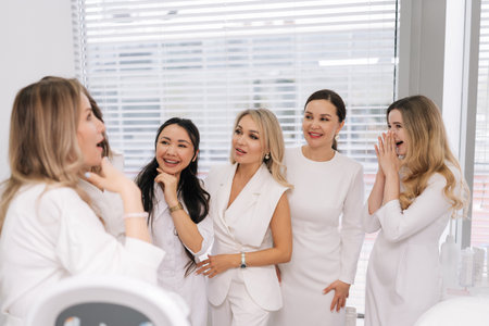 Happy five female healthcare professionals in white uniforms gathered together in modern clinic office, exchanging smiles as they discuss and share their expertise.の写真素材