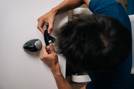 Close-up top view of technician male meticulously cleaning disassembled vertical mouse with...