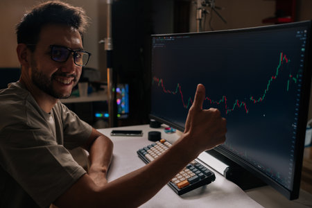 Happy trader male in home office gives thumbs up while viewing rising financial chart on computer...