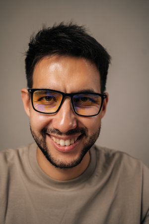 Headshot portrait of cheerful young man with beard and glasses smiling broadly looking at camera, expressing joy, success, confidence, reflecting positive attitude, wellbeing on isolated background.の写真素材
