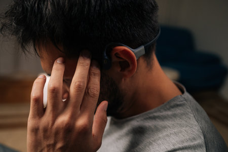 Close-up of man wearing bone conduction headphones, listening to audio content, interacting with device by touching temple, demonstrating modern wireless technology and convenient listening lifestyle.の写真素材