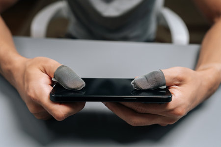 Close-up male hands wearing conductive finger sleeves on thumbs holding smartphone, improving touch screen sensitivity and grip for competitive mobile gaming and e-sports.の写真素材