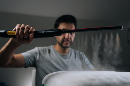 Front view man using handheld steam sterilizer tool for deep cleaning and disinfecting white memory foam pillow, ensuring hygiene and eliminating allergens from bedding. Concept of household chores.の写真素材